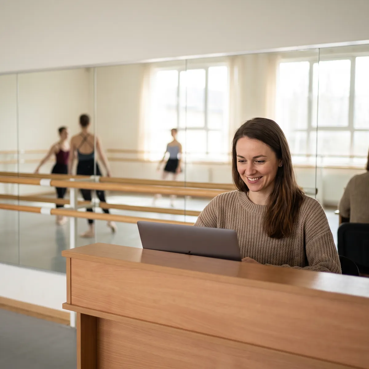 A studio owner at her front desk, smiling at a laptop.